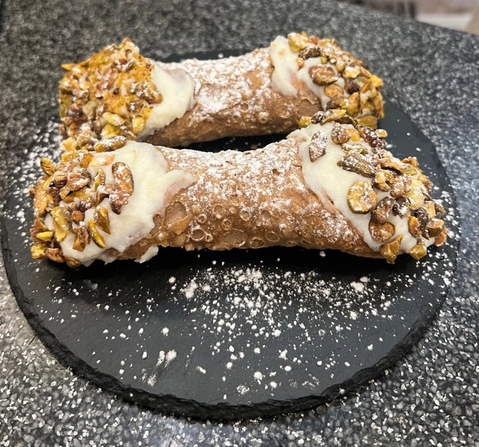 Zwei gefüllte Cannoli mit Pistazienstücken auf einer dunklen Platte