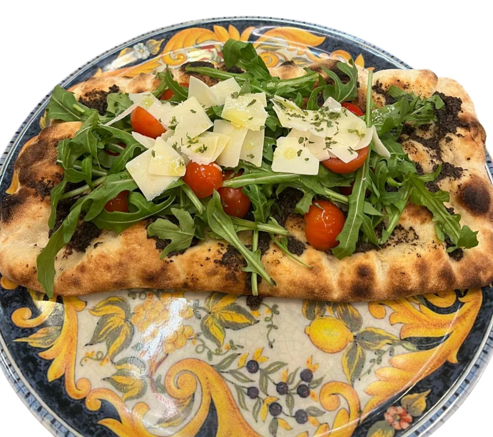 Pinsa mit Rucola, Tomaten und Parmesan auf einem bunten Teller